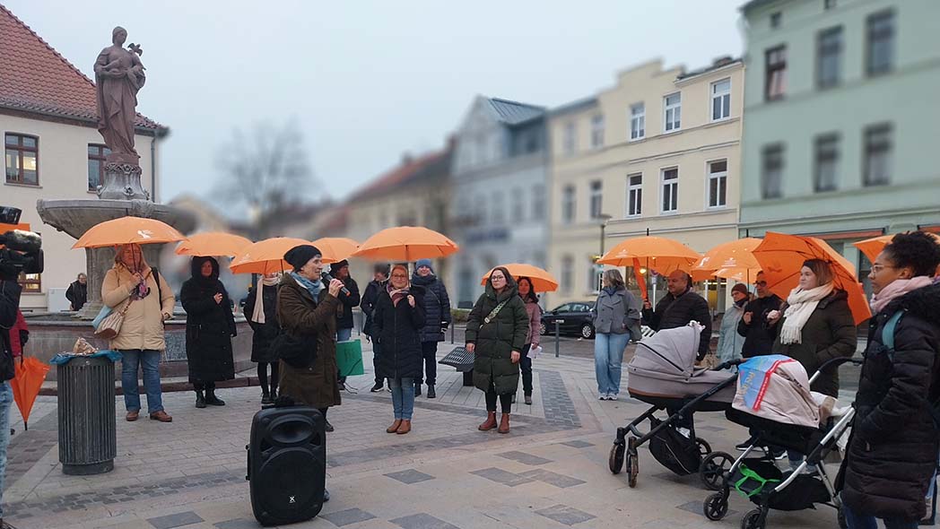 Frau spricht zu Gruppe mit orangefarbenen Regenschirmen