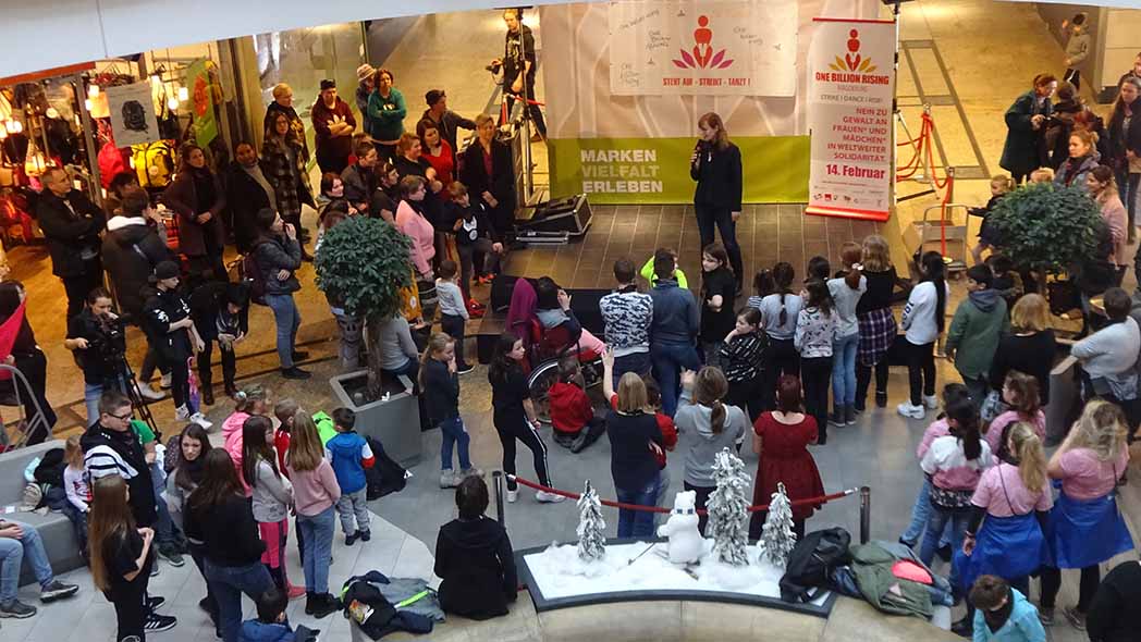 Einkaufscenter mit vielen Menschen vor einer Bühne.