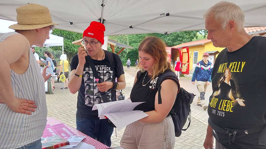 Drei Leute am Stand fragen eine Frau.